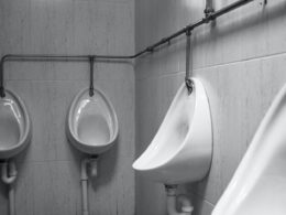 grayscale photography of four white ceramic urinal sinks